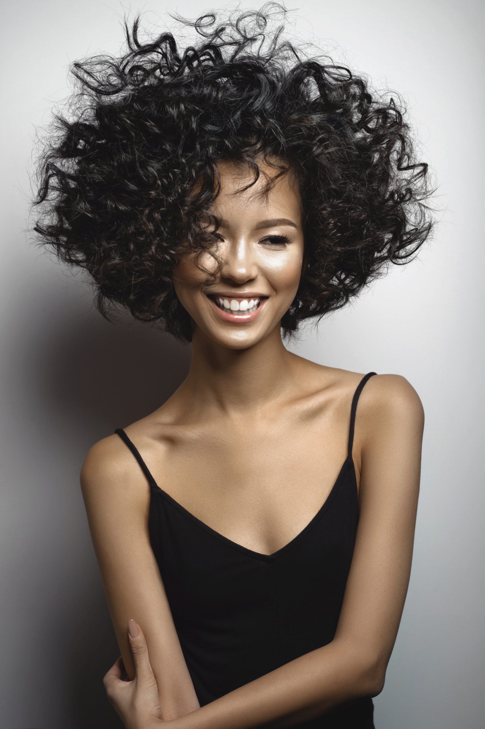 Fashion studio portrait of beautiful smiling woman in black dress with afro curls hairstyle. Fashion and beauty